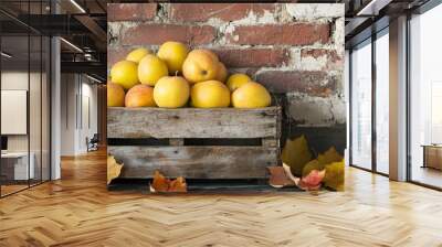 Quinces in a vintage wooden crate, placed against a worn brick wall with decorative fall leaves scattered around Wall mural