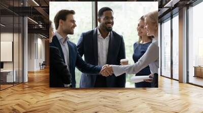 50s business lady shake hands greeting caucasian millennial businessman surrounded by multi ethnic businesspeople in formal suits. Sign contract express trust, partnership, start group meeting concept Wall mural