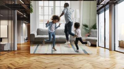 Active african funny dad little son and crazy daughter heavy metal or rock and roll lovers dancing in cozy living room relish life fooling around listening cool music scream with joy enjoy party hard Wall mural