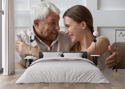 Adult granddaughter and old grandfather embracing sitting on couch indoors Wall mural