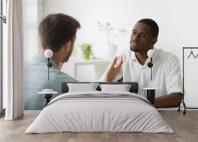 African American employer listening attentively to caucasian job applicant talking at work interview, being friendly and interested to candidate. Concept of recruiting, employment, hiring Wall mural