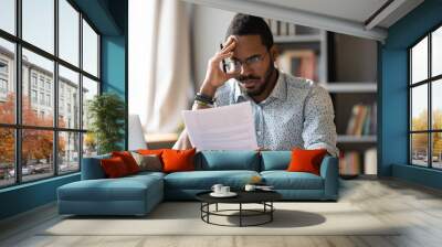 African American man wearing glasses dissatisfied by bad news received in letter, holding document, sitting at work desk, unexpected debt, bank or job dismissal notification, eviction notice Wall mural