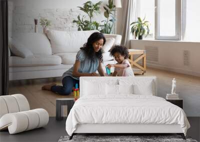 african mother and little girl play wooden colorful cubes, build towers sit on warm floor in living  Wall mural