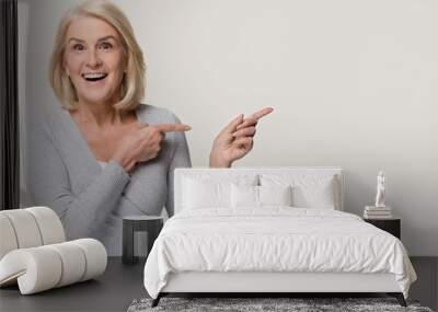 Amazed excited mature woman pointing at copyspace isolated on background Wall mural