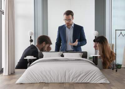 Angry male worker standing talking to colleagues lecturing on mistake in documents or failed project, businessman show dissatisfaction to business partner during negotiations or meeting in office Wall mural