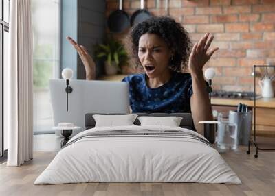 Angry young African American woman look at laptop screen distressed with slow internet connection. Mad biracial female frustrated by computer problem or spam working on gadget at home office. Wall mural