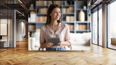 Attractive happy woman holding computer tablet, looking away. Pleasant smiling businesswoman distracted from job, planning workday. Dreamy young lady visualizing future, holding electronic gadget. Wall mural