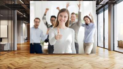 Attractive happy woman with group of multiracial millennial businesspeople on background standing smiling together in office with thumbs up looking at camera. Teamwork, collaboration approval concept Wall mural