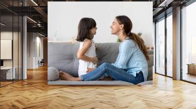 Attractive woman and little girl sitting on comfortable couch at home. Young mother talking communicates with small adorable daughter. Best friends happy motherhood weekend together with kid concept Wall mural