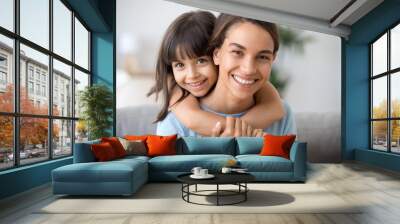 Beautiful family of single young mom and cute preschool kid daughter embracing mommy looking at camera, happy loving mother piggybacking smiling little child girl hugging mum headshot portrait Wall mural