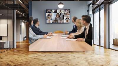 Business team of five sitting at meeting table in boardroom, talking to diverse group of freelance employees, workers on conference call, looking at set of head shots on large TV display Wall mural