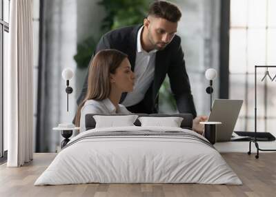 Businesswoman intern asking questions about online project to serious confident mentor, pointing at laptop screen, colleagues working together, discussing strategy, supervisor checking employee work Wall mural