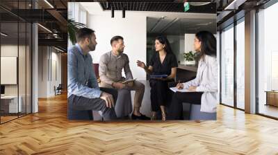 Busy diverse young colleagues meeting for communication, sitting in circle in co-working, discussing teamwork, common work tasks, project plan, strategy. Young business leader woman speaking to group Wall mural