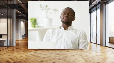 Calm satisfied African American businessman relaxing and meditating at workplace, having eyes closed, person practicing emotions control, preserving balance, managing stress. Peace, recovery concept Wall mural