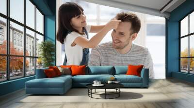 Caring happy preschool daughter brushing combing father hair. Wall mural