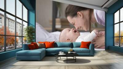 Cheerful adorable babygirl lying on bed enjoy loving mothers caress, close up side view face shot. Young woman touch her awakened baby looking at each other with warmth tender. Maternity, love concept Wall mural