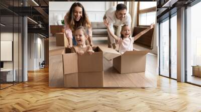 Cheerful adorable screaming girls sit inside of big carton boxes during race competition play with parents at new modern home at move day. Bank loan for young family, active games with kids concept Wall mural