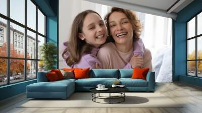 Cheerful affectionate teenage daughter hugging young mom looking at camera standing at home. Happy adult parent mother and cute teenage adolescent girl embracing, laughing. Close up family portrait Wall mural