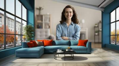 Cheerful confident gen Z young adult girl home head shot. Happy beautiful female student, freelance employee in casual posing in apartment with hands folded, looking at camera with toothy smile Wall mural