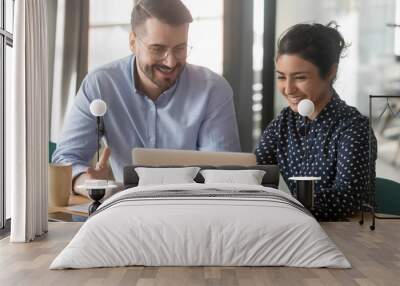 Cheerful hindu woman caucasian man multi-ethnic colleagues working together sit at desk look at computer screen discuss new project search solutions joking to increase effective communication concept Wall mural