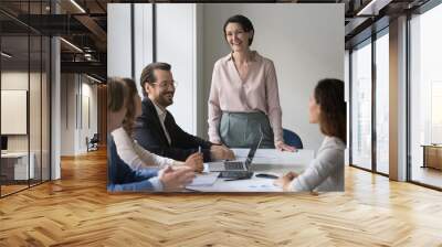 Cheerful mature female boss speaking to successful millennial professional team of corporate meeting, discussing business project, brainstorming on ideas, laughing, having fun Wall mural