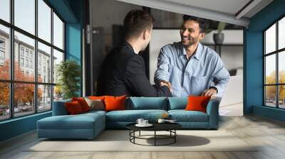 Cheerful multiethnic male business partners shaking hands at workplace table, smiling, laughing, finishing conversation, negotiation, consultation meeting, discussing cooperation, partnership Wall mural