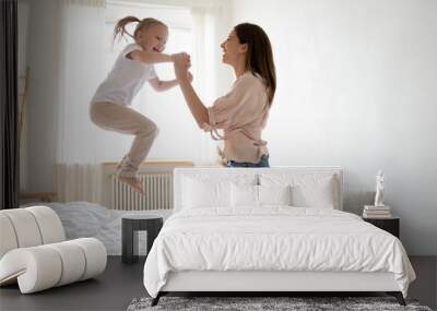 Cheerful mum play with active kid girl jump on bed Wall mural