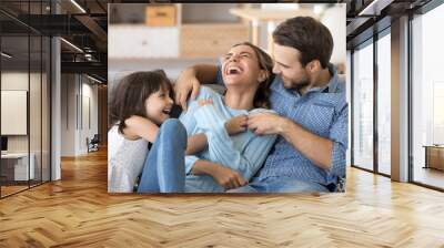 Cheerful people sitting on couch in living room have fun little daughter tickling mother laughing together with parents enjoy free time playing at home. Weekend activity happy family lifestyle concept Wall mural