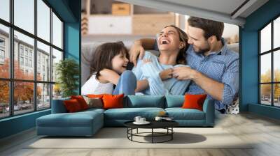 Cheerful people sitting on couch in living room have fun little daughter tickling mother laughing together with parents enjoy free time playing at home. Weekend activity happy family lifestyle concept Wall mural