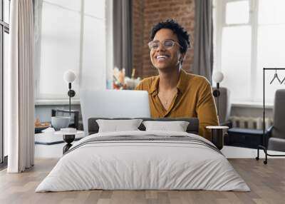 Cheerful short haired African employee sitting at workplace with laptop in office, typing, looking at camera, smiling, laughing. Millennial worker, working business woman in casual head shot portrait Wall mural