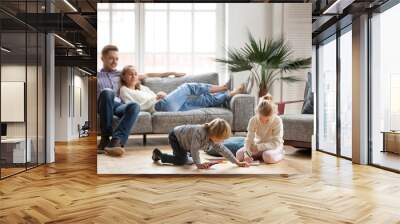 Children sister and brother playing drawing together on floor while young parents relaxing at home on sofa, little boy girl having fun, friendship between siblings, family leisure time in living room Wall mural