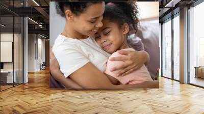 Close up diverse happy mother holding flowers, bouquet and gift embracing little daughter, congratulate young african american mom with mothers day or birthday, adorable child making surprise to mum. Wall mural