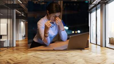 Close up exhausted Indian businesswoman taking off glasses, massaging nose bridge, suffering from eye strain, dry eyes syndrome, using laptop, working, finishing project at night, deadline concept Wall mural