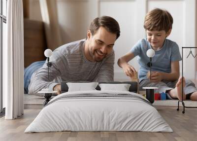 Close up happy loving father playing with adorable son at home, lying on warm floor, smiling dad and little boy kid constructing with wooden colorful blocks, enjoying leisure time in living room Wall mural