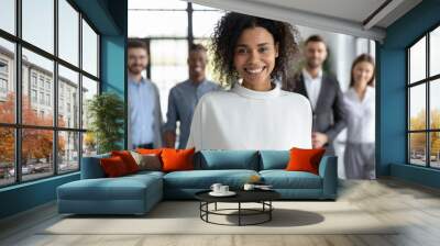 Close up headshot portrait of happy african american businesswoman looking at camera. Different smiling businesspeople standing behind of female company mentor. Leader of multi-ethnic team concept. Wall mural