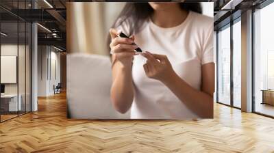 Close up image, young woman sitting on couch at home holding portable glucose meter electronic device checkup test blood sugar. Patient with diabetes mellitus health problem, modern tool usage concept Wall mural