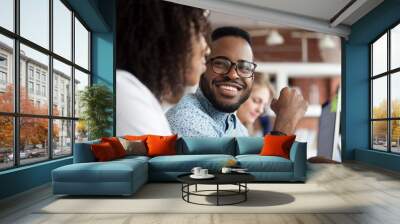 Close up of smiling African American employee look at female colleague chatting in office, happy black male worker talk with woman coworker, having casual conversation at workplace, have fun Wall mural