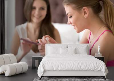 Close up portrait of pretty young woman painting nails with her girlfriend on blurred background using nail file. Female friends do manicure procedures when spending time together and chatting at home Wall mural