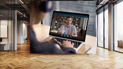 Close up rear view of female employee have webcam virtual digital conference with male colleague on computer. Woman talk on video call with coworker, engaged in online team meeting on laptop. Wall mural