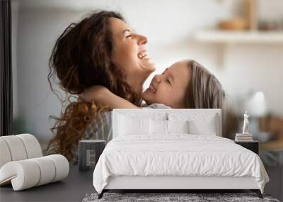 Close up side view overjoyed smiling young mother and daughter hugging and laughing, enjoying tender moment, happy mum and adorable preschool girl kid cuddling, having fun together at home Wall mural