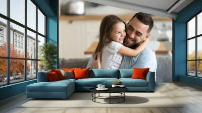 Close up smiling loving young father hugging adorable little daughter, enjoying tender moment, spending weekend together, sitting on cozy couch at home, good family relationship between dad and child Wall mural