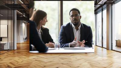 Concentrated black team leader posing problem to employees, afro-american coach or mentor setting target to group of trainees, manager discussing his business idea with diverse colleagues on meeting Wall mural