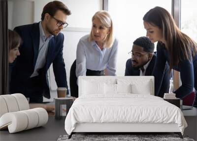 Concentrated diverse businesspeople talk brainstorm at team meeting discussing paperwork together. Focused multiracial colleagues analyze financial documents at briefing in office. Teamwork concept. Wall mural