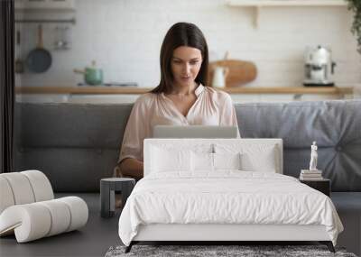 concentrated millennial girl sit on couch working on laptop browsing internet at home during lazy we Wall mural