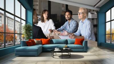 Confident blonde elder business woman talking to diverse younger coworkers at corporate meeting, speaking at large table, discussing creative ideas for brainstorming Wall mural