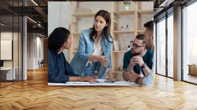 Confident businesswoman team leader speaking, training staff at meeting, diverse colleagues employees working with statistics, financial documents together, coworkers group engaged in teamwork Wall mural