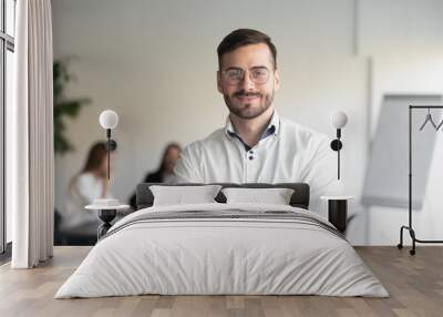 Confident happy young male manager in eyeglasses standing with folded hands head shot portrait. Smiling company owner, startup businessman, team leader, successful employee looking at camera. Wall mural