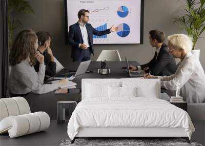 Confident young business leader man presenting marketing statistic report to partners, investors, selling startup project on meeting, negotiations, showing graphs on electronic display Wall mural