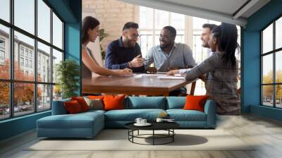 Diverse employees sitting at table having pleasant positive conversation Wall mural