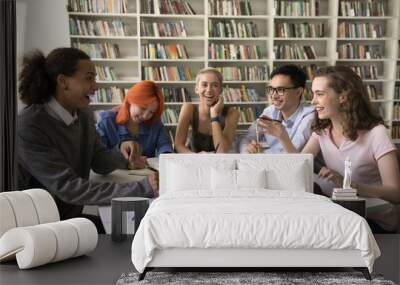 Diverse group of cheerful classmates brainstorming on common studying project in campus library, discussing homework, education, research, chatting, talking, laughing, having fun Wall mural